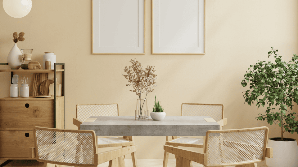 A modern dining area featuring a Nostaloft dining table with a minimalist concrete top and stylish wooden chairs, complemented by a warm yellow wall, decorative plants, and chic shelving units.